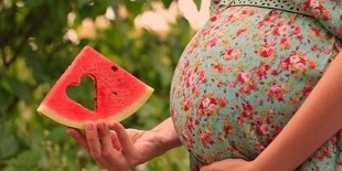 slice of watermelon in the hands of a pregnant woman